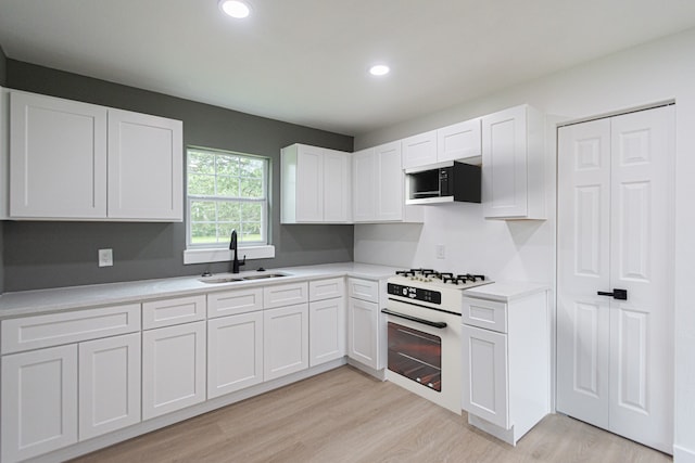 kitchen with white cabinetry, white appliances, light hardwood / wood-style flooring, and sink