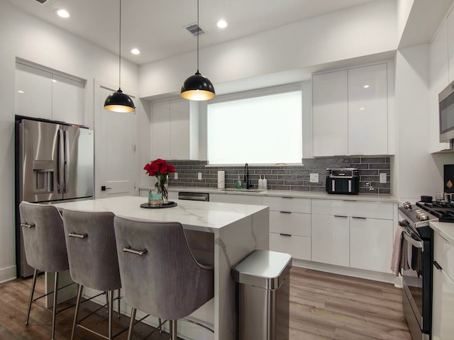 kitchen featuring a center island, sink, white cabinets, hanging light fixtures, and appliances with stainless steel finishes