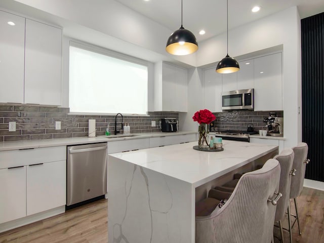 kitchen with appliances with stainless steel finishes, white cabinets, a kitchen island, pendant lighting, and sink