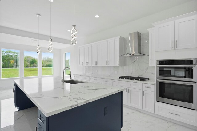 kitchen featuring wall chimney range hood, decorative backsplash, an island with sink, and white cabinetry