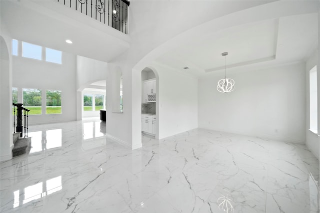 empty room with a towering ceiling, a raised ceiling, and light tile patterned floors