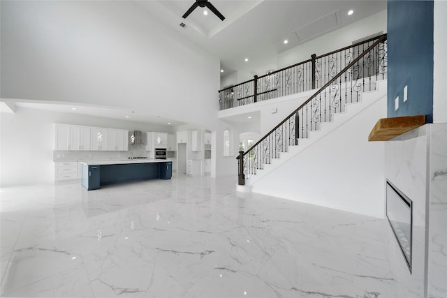 unfurnished living room with a towering ceiling, ceiling fan, and light tile patterned flooring