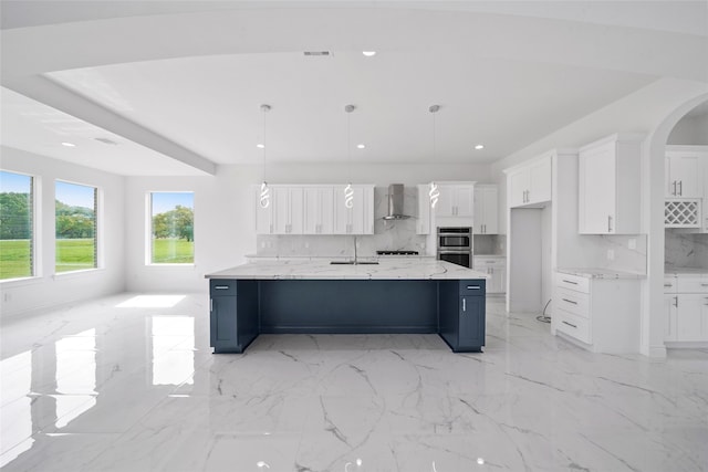 kitchen with white cabinetry, a spacious island, decorative backsplash, and wall chimney range hood