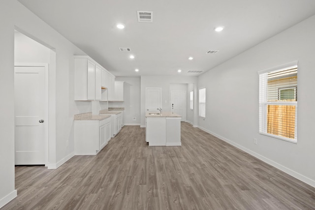 kitchen with light wood-type flooring, a center island with sink, and white cabinetry