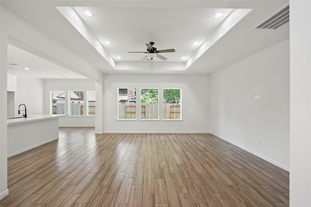 unfurnished living room featuring a tray ceiling, a healthy amount of sunlight, hardwood / wood-style floors, and ceiling fan