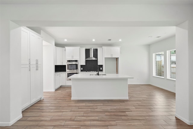 kitchen with white cabinetry, backsplash, double oven, and a kitchen island with sink