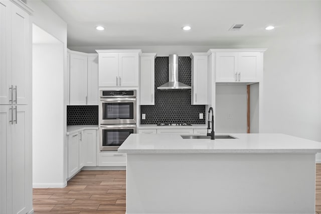 kitchen with an island with sink, wall chimney exhaust hood, and tasteful backsplash