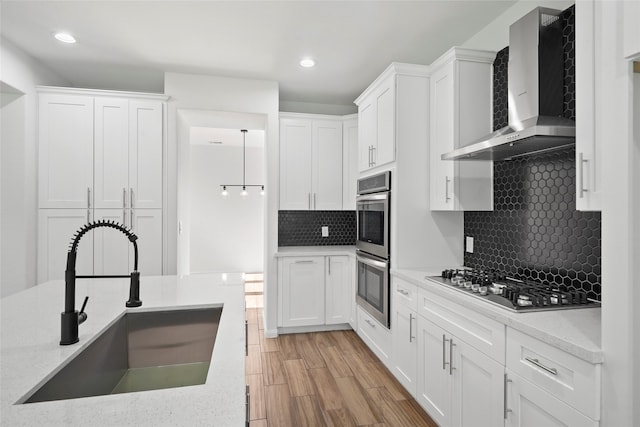 kitchen with light hardwood / wood-style flooring, stainless steel appliances, sink, wall chimney exhaust hood, and decorative backsplash