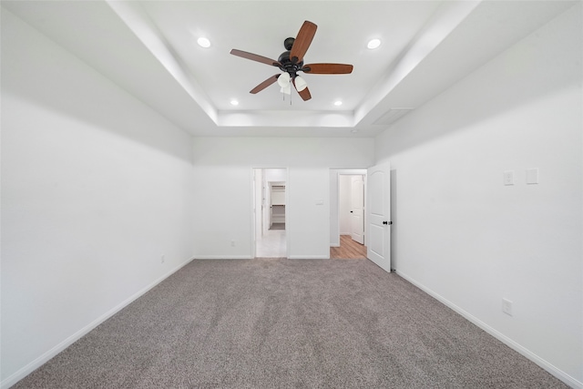 unfurnished bedroom featuring light colored carpet, a closet, a tray ceiling, a spacious closet, and ceiling fan