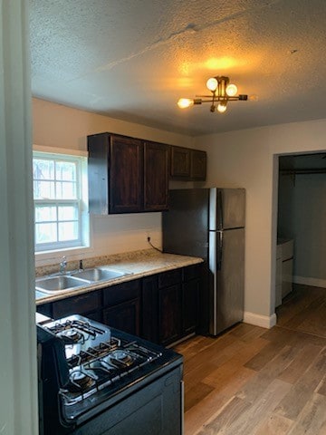 kitchen with light hardwood / wood-style flooring, sink, stainless steel fridge, dark brown cabinets, and black range oven