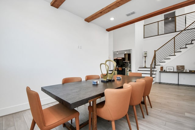 dining area featuring a towering ceiling, beamed ceiling, and light hardwood / wood-style flooring