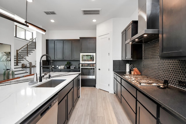 kitchen featuring appliances with stainless steel finishes, tasteful backsplash, sink, wall chimney range hood, and light wood-type flooring