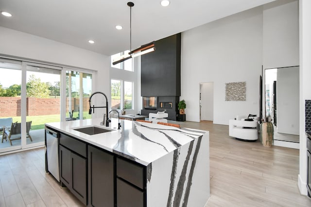 kitchen featuring a towering ceiling, an island with sink, sink, and light hardwood / wood-style floors