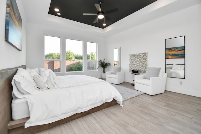 bedroom with a raised ceiling, ceiling fan, and light hardwood / wood-style flooring