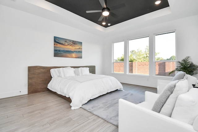 bedroom with ceiling fan, a tray ceiling, and light hardwood / wood-style floors