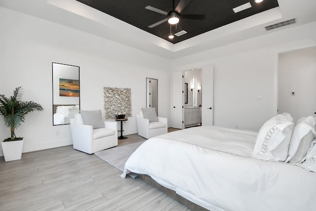 bedroom featuring light hardwood / wood-style floors, ceiling fan, a raised ceiling, and ensuite bathroom