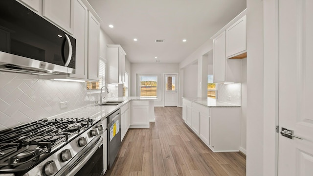 kitchen with white cabinets, sink, light wood-type flooring, appliances with stainless steel finishes, and light stone counters