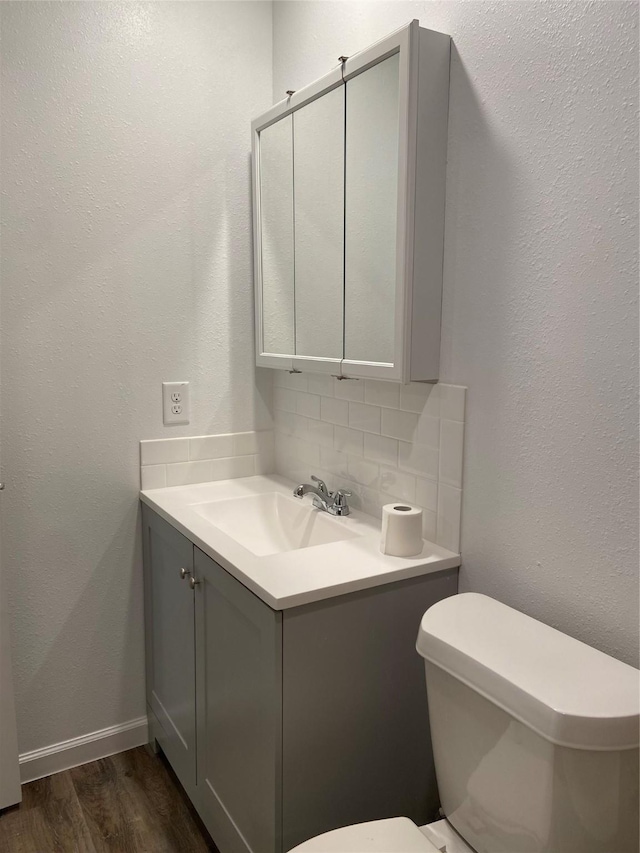 half bathroom with tasteful backsplash, toilet, vanity, wood finished floors, and baseboards