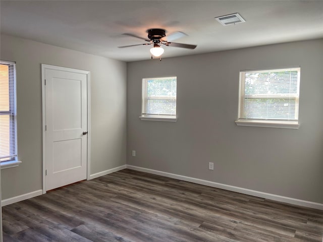 spare room featuring dark wood-type flooring, a ceiling fan, visible vents, and baseboards