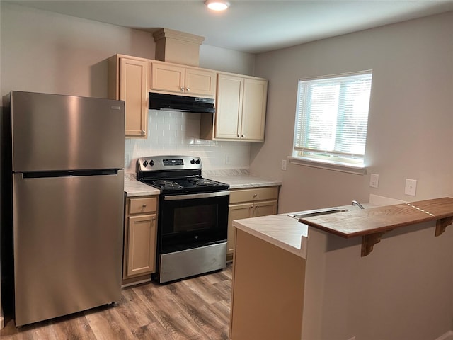 kitchen with appliances with stainless steel finishes, a peninsula, light wood-type flooring, under cabinet range hood, and a kitchen breakfast bar