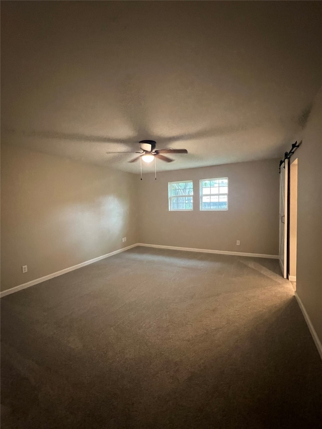 carpeted spare room with a barn door and ceiling fan