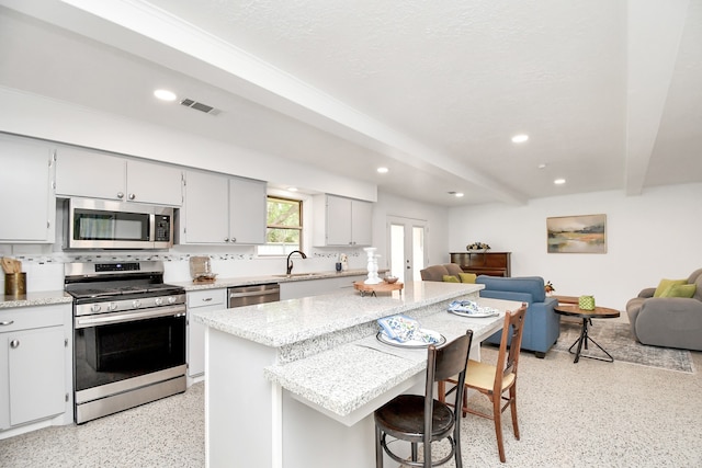 kitchen featuring a kitchen island, appliances with stainless steel finishes, backsplash, a breakfast bar area, and sink