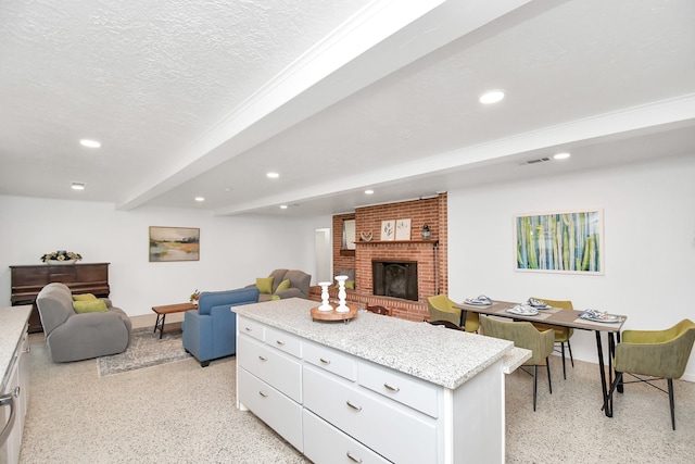 kitchen featuring beam ceiling, a kitchen island, white cabinetry, a textured ceiling, and a brick fireplace