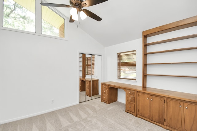 unfurnished office featuring built in desk, light carpet, a wealth of natural light, and ceiling fan