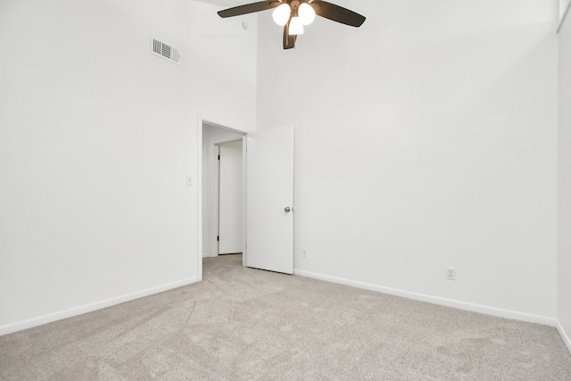 carpeted empty room featuring ceiling fan and a high ceiling