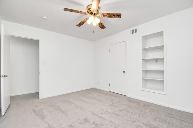 unfurnished room featuring light carpet, built in shelves, and ceiling fan