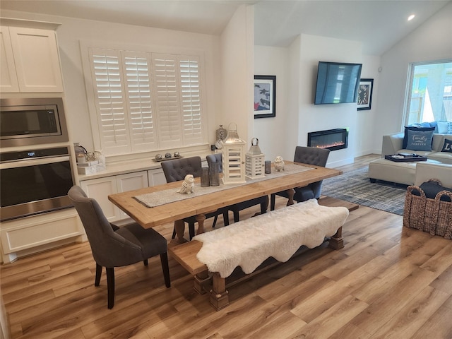 dining space featuring recessed lighting, light wood-style flooring, a glass covered fireplace, and vaulted ceiling