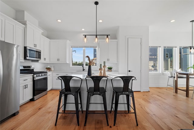 kitchen with appliances with stainless steel finishes, light wood-type flooring, white cabinets, a kitchen island, and hanging light fixtures