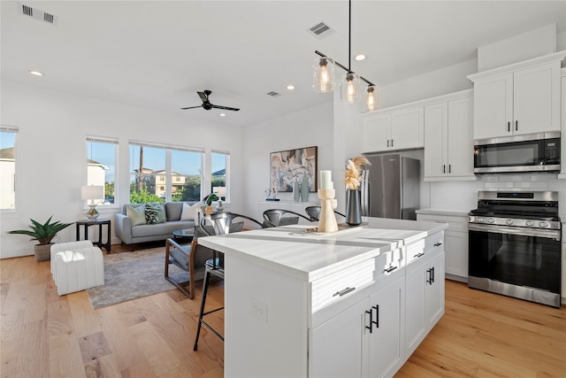 kitchen featuring white cabinets, appliances with stainless steel finishes, light wood-type flooring, and a kitchen island