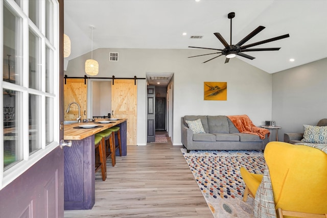 living room with a barn door, sink, ceiling fan, wood-type flooring, and high vaulted ceiling