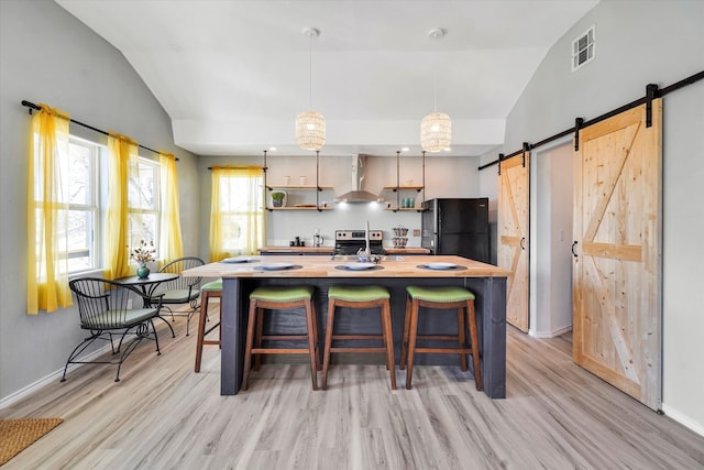 kitchen featuring black fridge, light hardwood / wood-style floors, lofted ceiling, a barn door, and wall chimney range hood