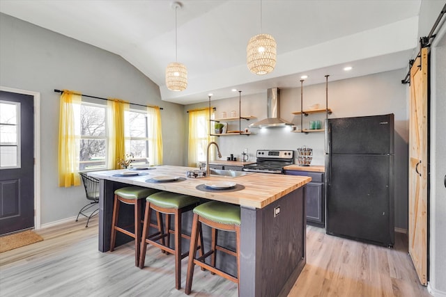 kitchen featuring stainless steel electric stove, butcher block countertops, black fridge, a barn door, and wall chimney range hood