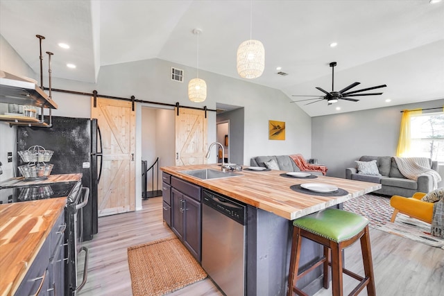 kitchen with a barn door, wooden counters, stainless steel appliances, and ceiling fan