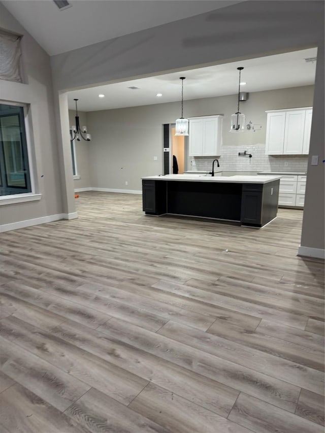 kitchen with light wood-type flooring, white cabinetry, and a kitchen island with sink