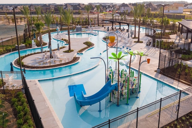 community pool featuring a water play area, a residential view, a water slide, and fence