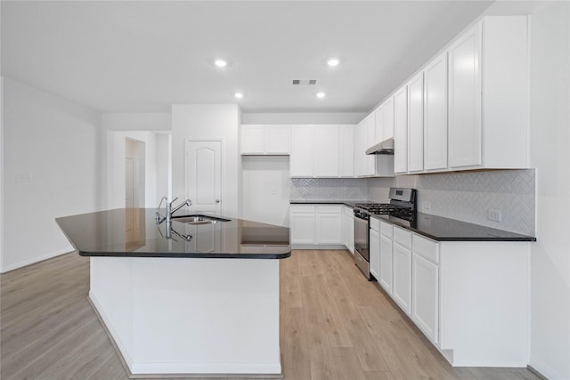 kitchen featuring a sink, stainless steel gas range, dark countertops, visible vents, and under cabinet range hood