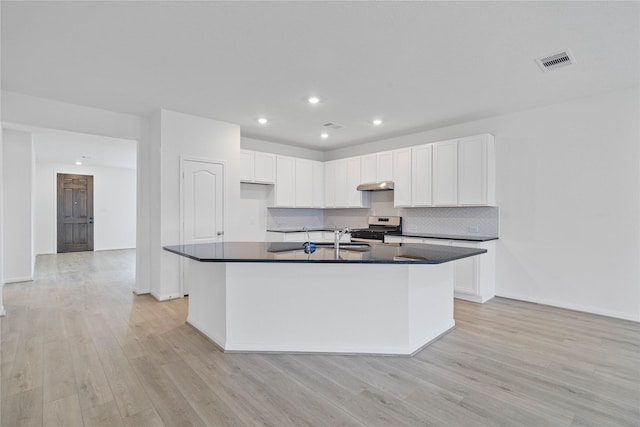 kitchen with stainless steel range with gas cooktop, light wood-style flooring, under cabinet range hood, and dark countertops