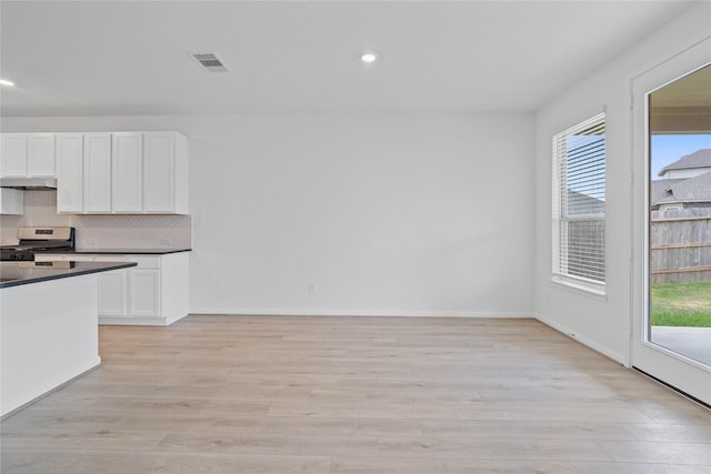 kitchen with dark countertops, white cabinets, under cabinet range hood, gas stove, and visible vents