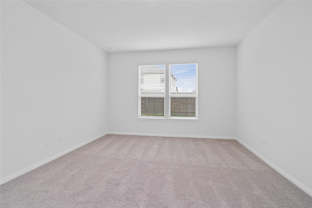 spare room featuring light carpet and baseboards