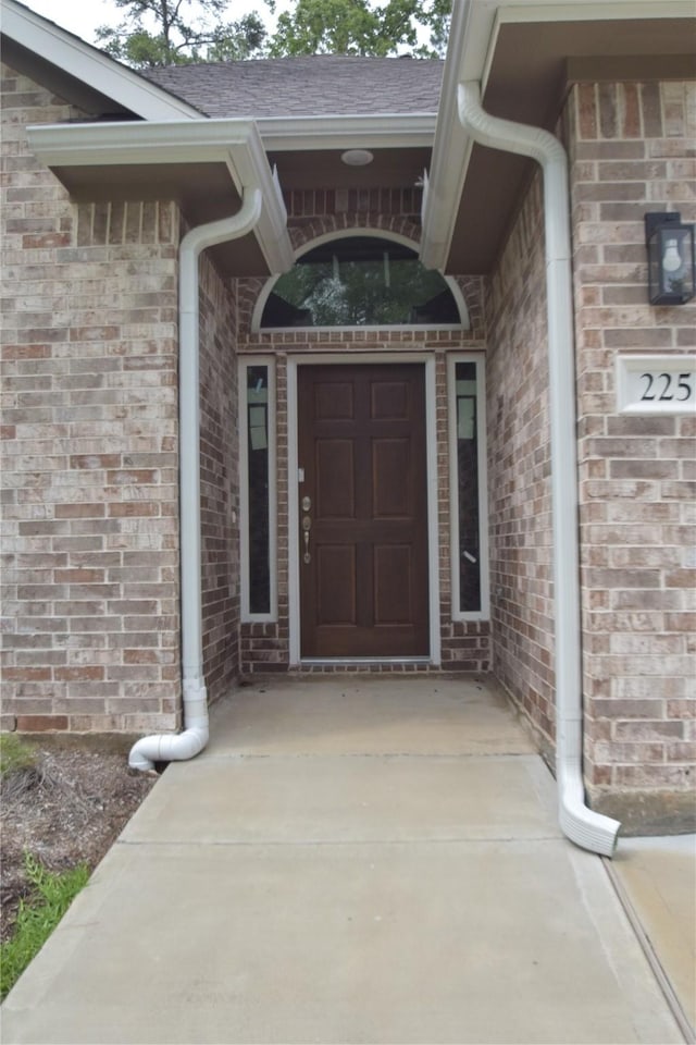 entrance to property featuring brick siding and roof with shingles