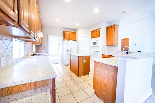 kitchen featuring light tile patterned flooring, a peninsula, white appliances, a sink, and a center island