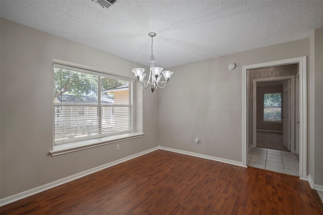 spare room with a textured ceiling, dark hardwood / wood-style flooring, plenty of natural light, and an inviting chandelier