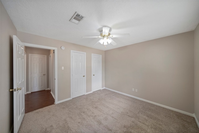 unfurnished bedroom featuring a textured ceiling, two closets, carpet, and ceiling fan