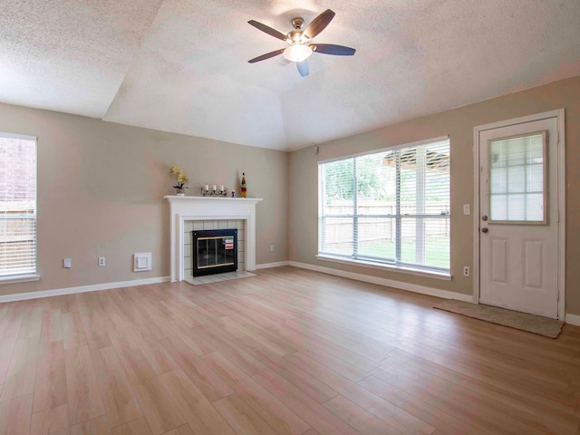 unfurnished living room with light hardwood / wood-style flooring, a textured ceiling, a tile fireplace, and ceiling fan