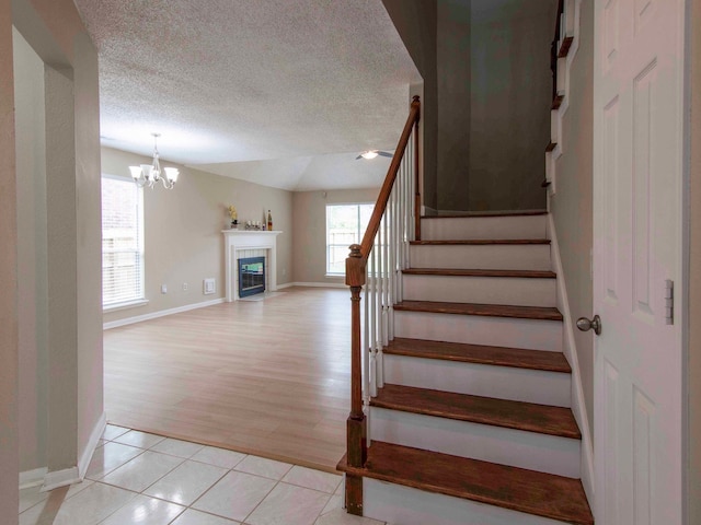 stairs with a textured ceiling, a chandelier, wood-type flooring, and a fireplace