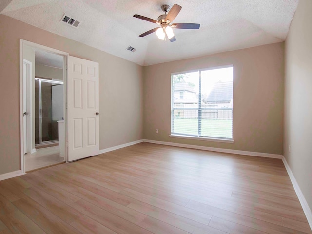 empty room featuring light hardwood / wood-style floors, a textured ceiling, and vaulted ceiling